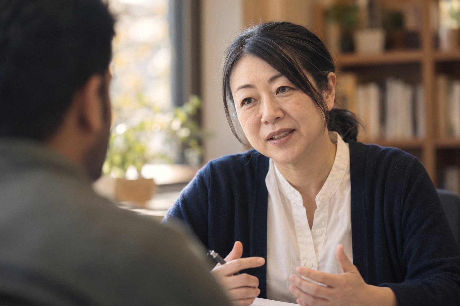 机をはさんで、相談に来た人に話しかける所長の佐伯。手前に相談者の後ろ姿
